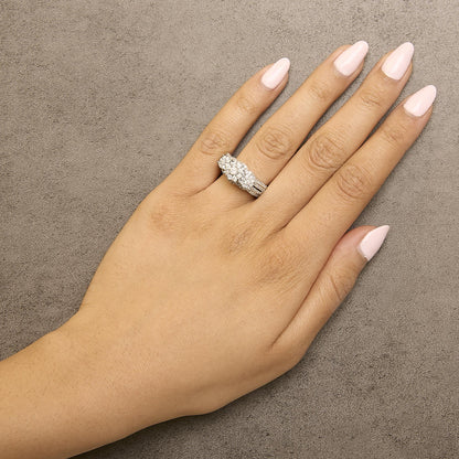 Close-up top view of a model's hand wearing a white metal ring featuring one larger round white gemstone in prong setting, flanked by multiple smaller round white gemstones in prong settings.