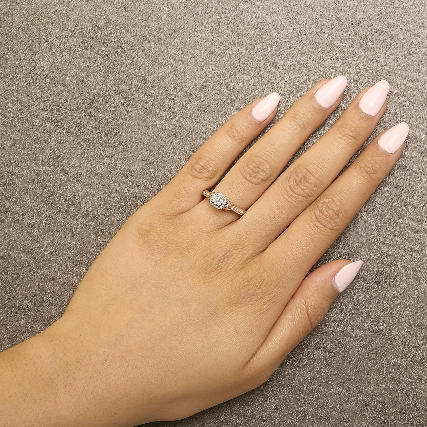 Rose and white metal ring with cluster of round white gemstones in prong setting, shown worn on a model's hand from above.
