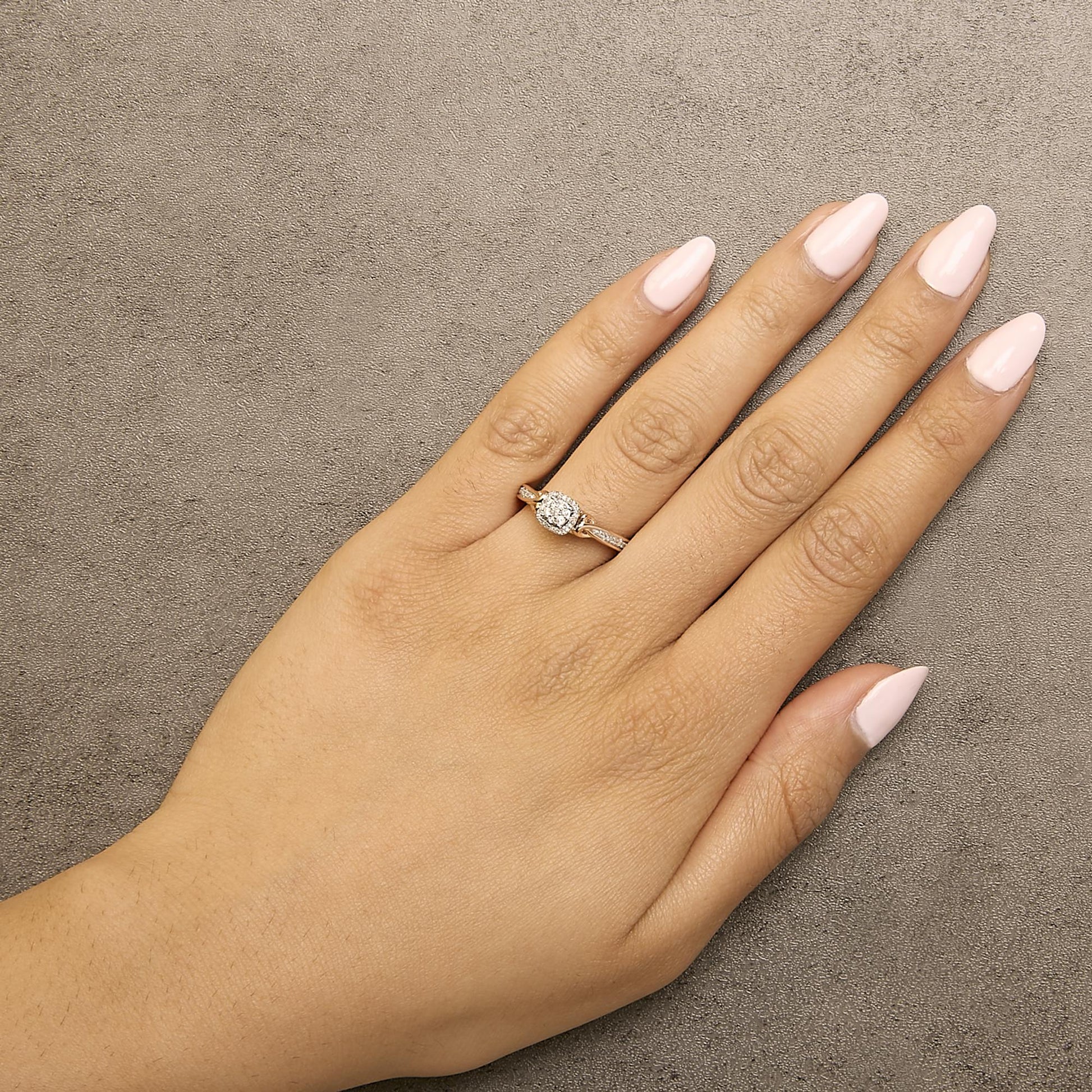 Rose and white metal ring with cluster of round white gemstones in prong setting, shown worn on a model's hand from above.