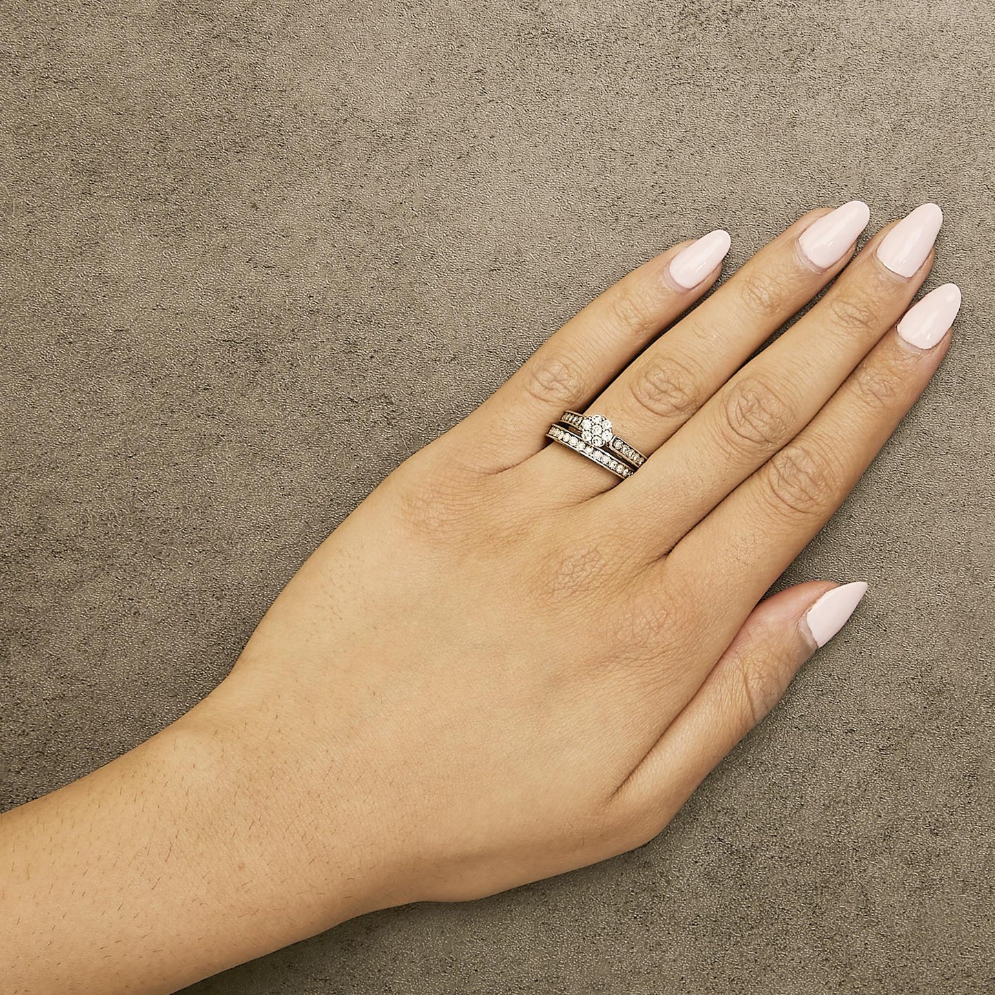 Close-up top view of a model's hand wearing a white metal ring set featuring round white gemstones in prong settings.