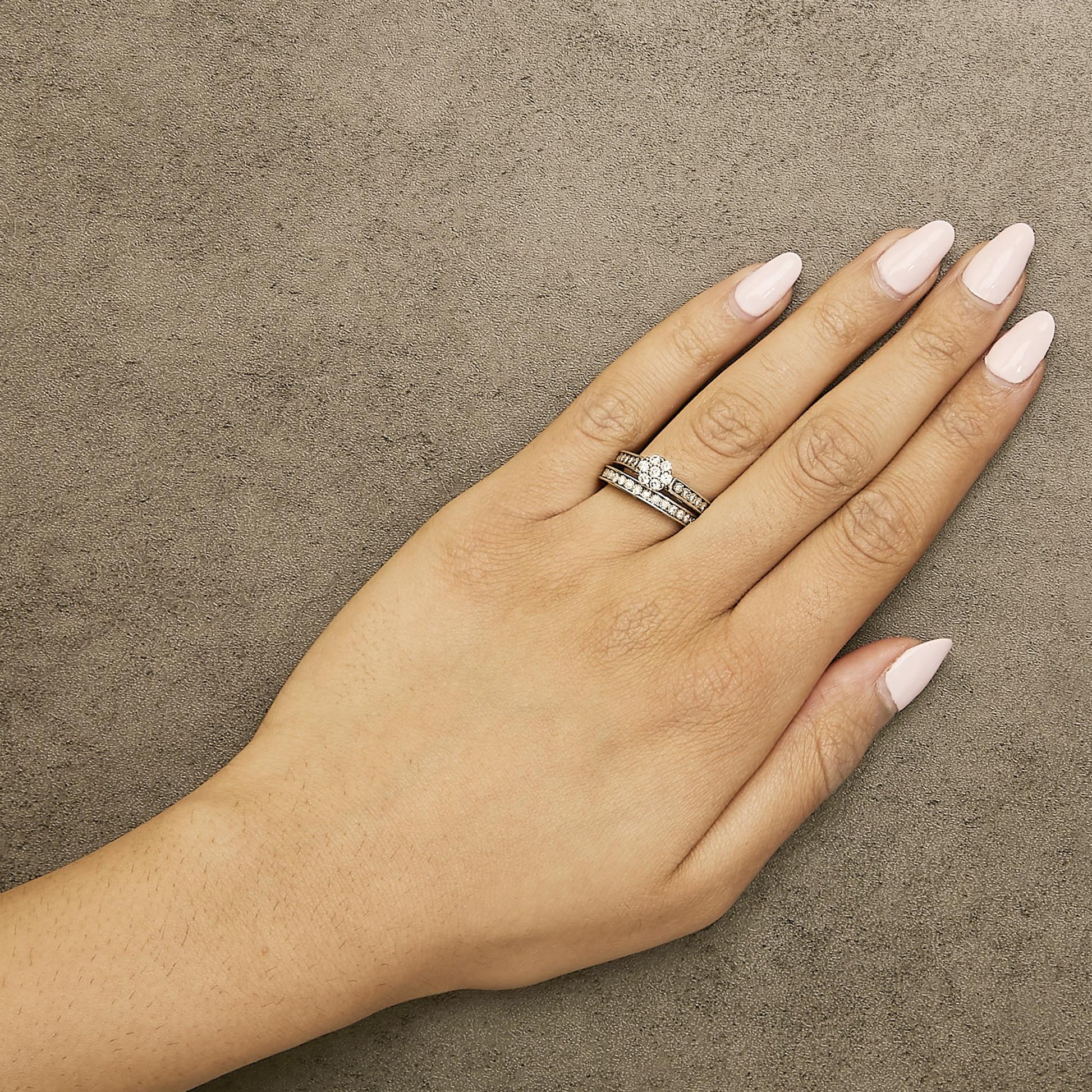 Close-up top view of a model's hand wearing a white metal ring set featuring round white gemstones in prong settings.