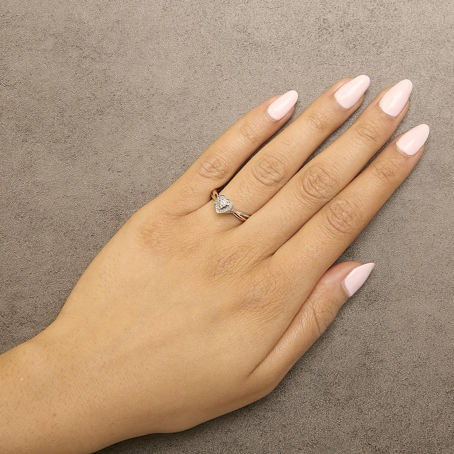 Ring with a heart-shaped cluster of white round gemstones in prong settings on a two-tone band, shown worn on a model's hand from a top angle.