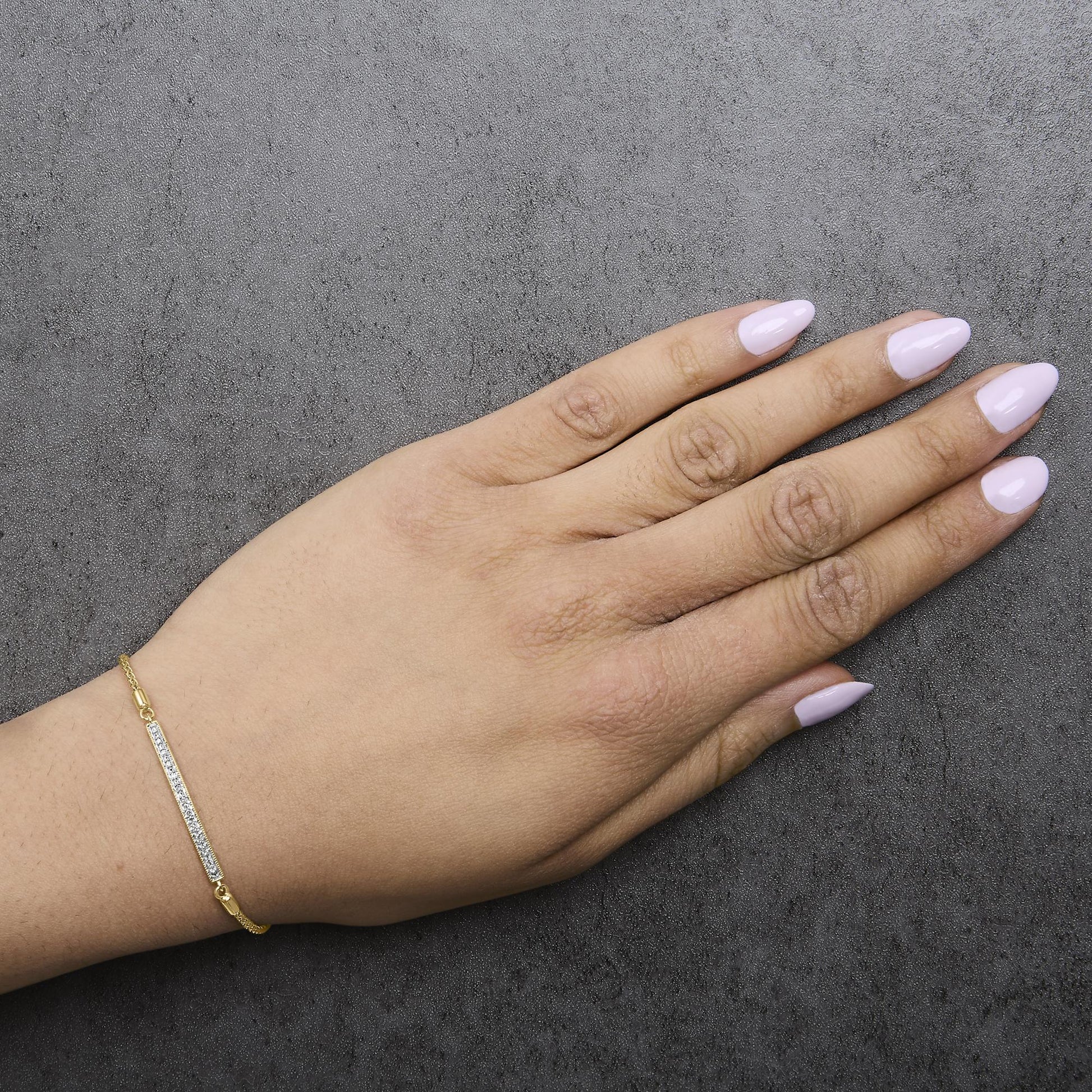 Yellow metal bracelet with a rectangular bar featuring small white gemstones in pave setting, shown worn on a model's wrist from top angle.