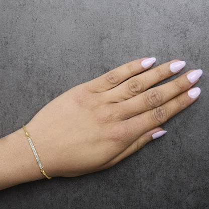 Yellow metal bracelet with a rectangular bar featuring small white gemstones in pave setting, shown worn on a model's wrist from top angle.