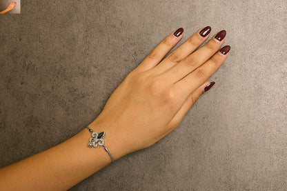 White metal bracelet with a decorative centerpiece featuring a black marquise-shaped gemstone and an orange marquise-shaped gemstone, surrounded by small white round gemstones in a pave setting, shown worn on a model's wrist from a top-down angle.