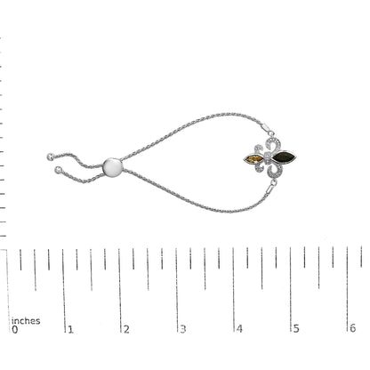 White metal bracelet shown on a scale, featuring a fleur-de-lis design with two marquise-shaped bezel-set gemstones in black and orange colors, surrounded by small round white pave-set gemstones, photographed from above.