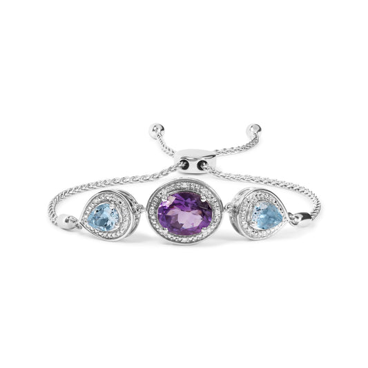 White bracelet with a central oval purple gemstone and two pear-shaped blue gemstones on either side, all surrounded by small round white gemstones, shown in a front-facing angle.