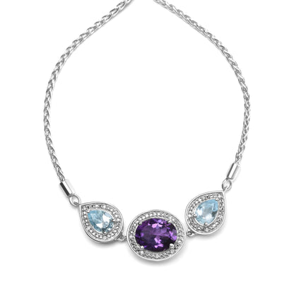 White metal bracelet with a central oval purple gemstone and two pear-shaped blue gemstones on either side, each surrounded by small round white gemstones, shown in a flat lay front angle.