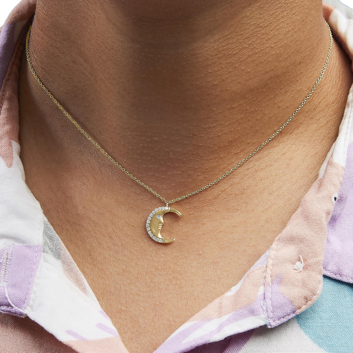 Close-up front view of a yellow metal necklace with a crescent moon pendant adorned with white round gemstones, worn on a model.