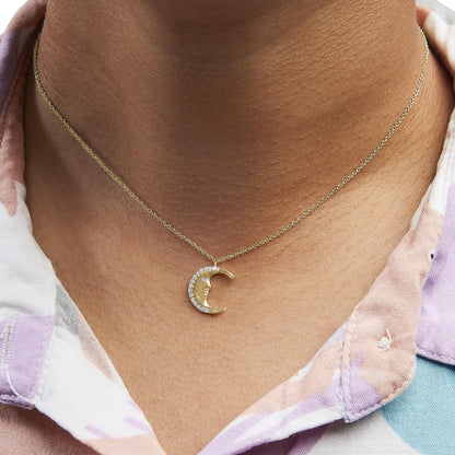Close-up front view of a yellow metal necklace with a crescent moon pendant adorned with white round gemstones, worn on a model.