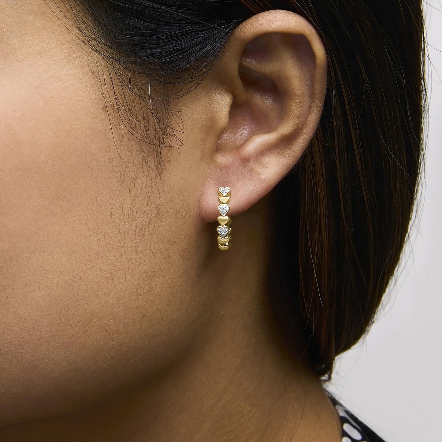 Close-up side view of a model wearing yellow metal hoop earrings with white gemstones in a pave setting.