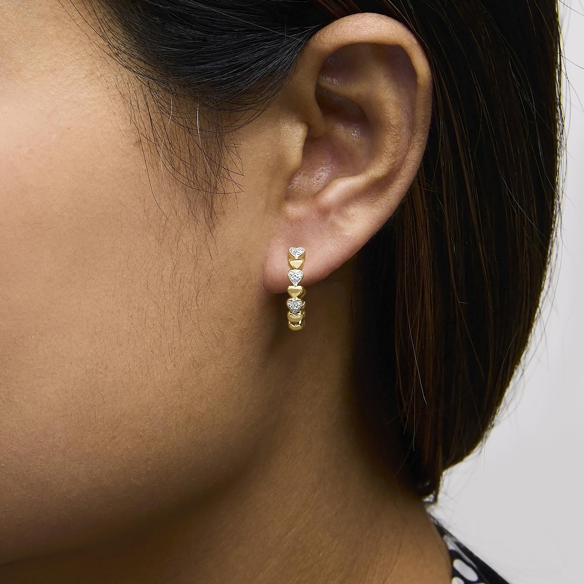 Close-up side view of a model wearing yellow metal hoop earrings with white gemstones in a pave setting.