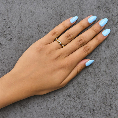 Yellow metal ring with alternating heart shapes and white gemstones in pave setting, shown worn on a model's finger, top-down angle.