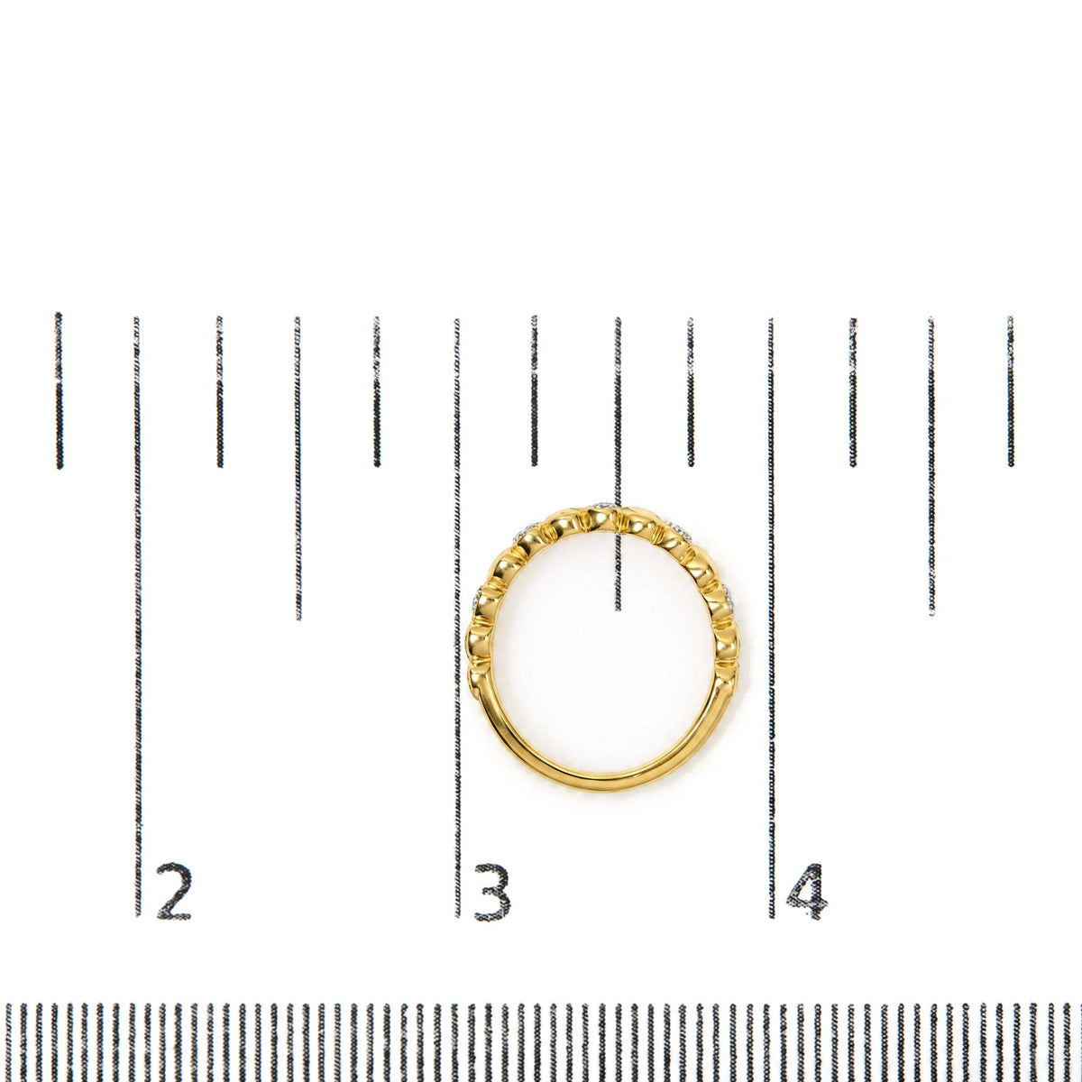 Close-up top view of a yellow-colored ring with evenly spaced raised rounded segments, shown on a scale with white gemstones in a pave setting around the outer edge.