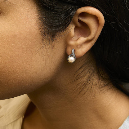 Close-up side view of a model wearing white earrings with a round pearl and curved design featuring round white gemstones in pave setting.