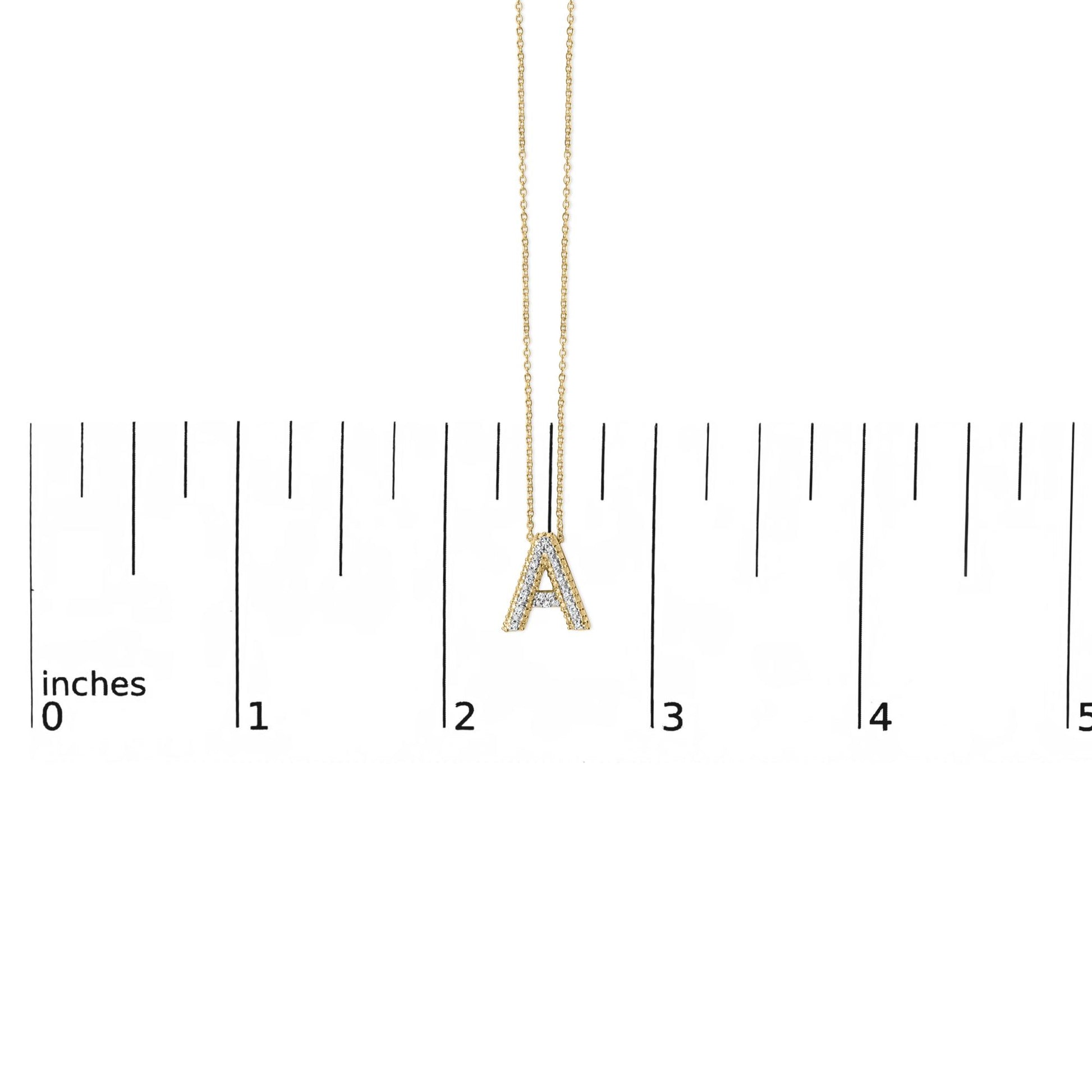 Close-up front view of a yellow metal necklace with a pendant shaped like the letter 'A,' adorned with white round gemstones in prong settings, shown on a scale.