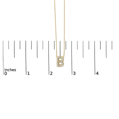 Close-up front view of a yellow necklace pendant shaped like the letter B, adorned with white gemstones in a prong setting, shown on a scale.