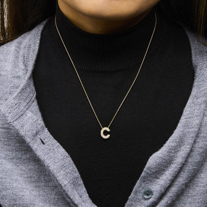 Close-up front view of a model wearing a yellow metal necklace with a pendant shaped like the letter 'C' adorned with round white gemstones in prong settings.