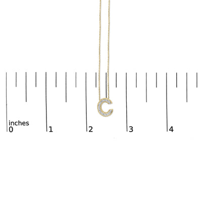 Yellow necklace with a pendant shaped like the letter C, outlined with white gemstones in prong settings, shown on a scale with an overhead angle.