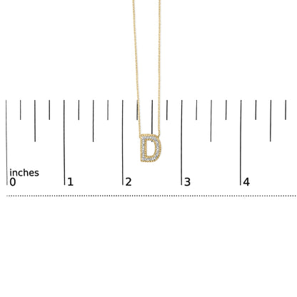 Close-up front view of a yellow necklace with a D-shaped pendant outlined with white gemstones, shown on a scale.
