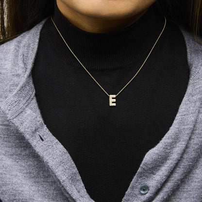 Close-up front view of a model wearing a yellow metal necklace with a pendant in the shape of the letter E, encrusted with white gemstones in a prong setting.