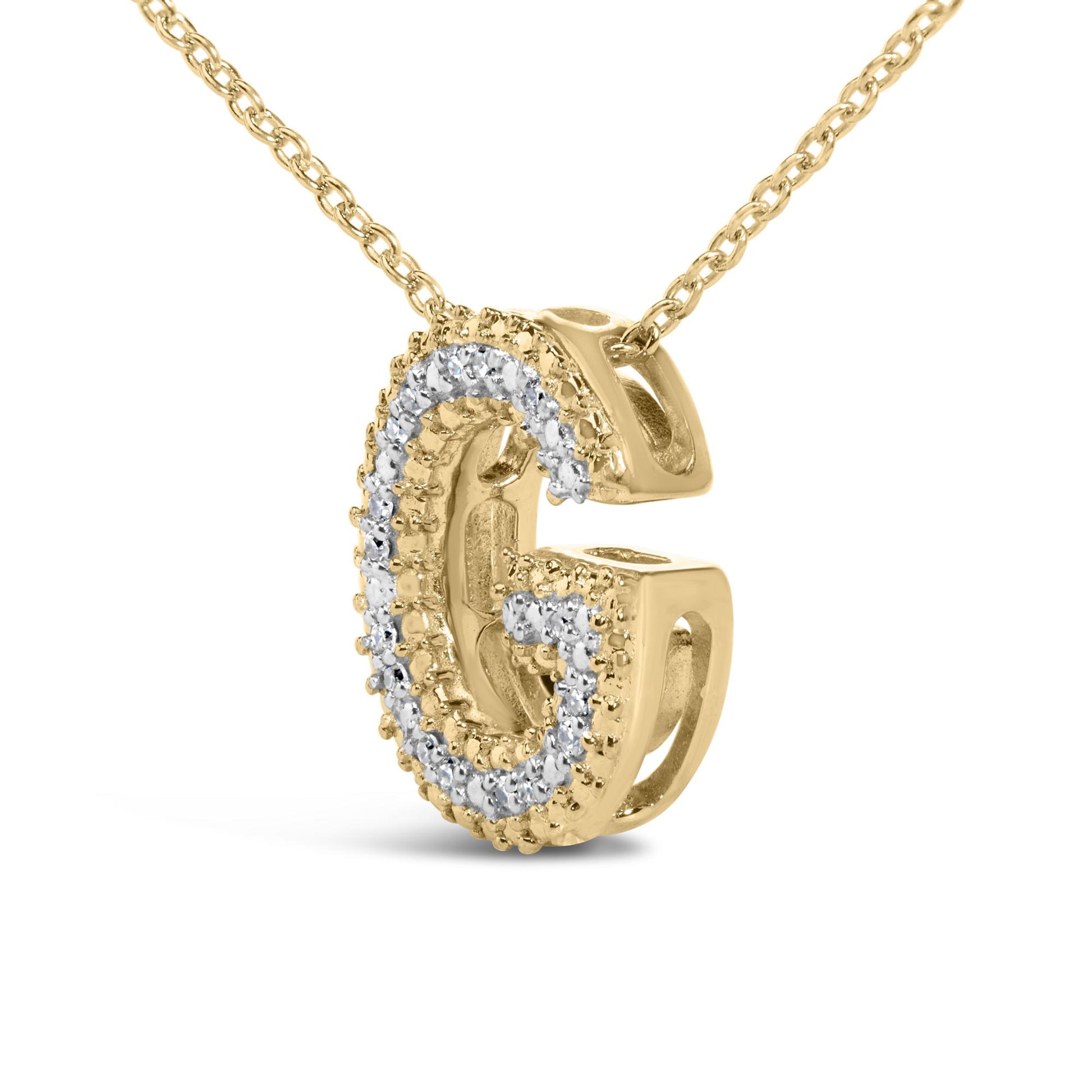 Close-up front angle of a yellow metal necklace pendant in the shape of the letter G, adorned with white round prong-set gemstones along the front surface, shown on a white background.