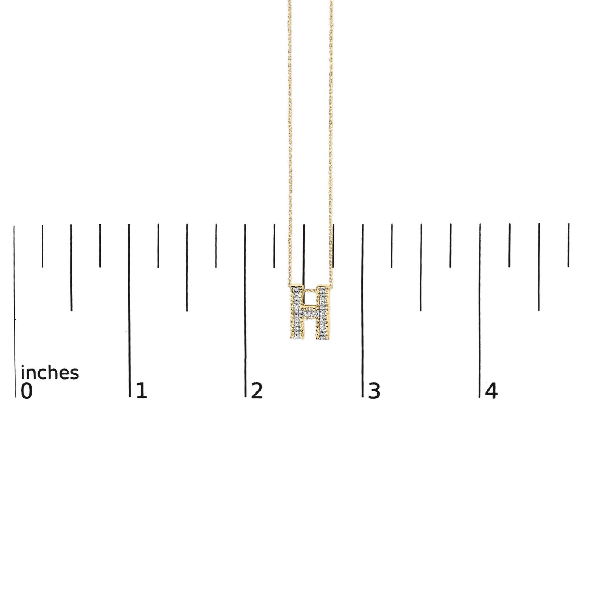 Yellow necklace with an H-shaped pendant adorned with round white gemstones in prong settings, shown on a scale, front view.