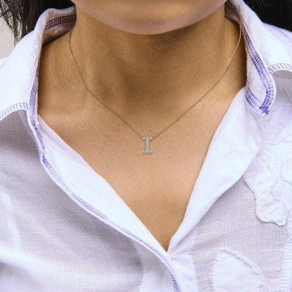 Close-up front view of a model wearing a yellow metal necklace with an I-shaped pendant encrusted with multiple small white gemstones in prong settings.