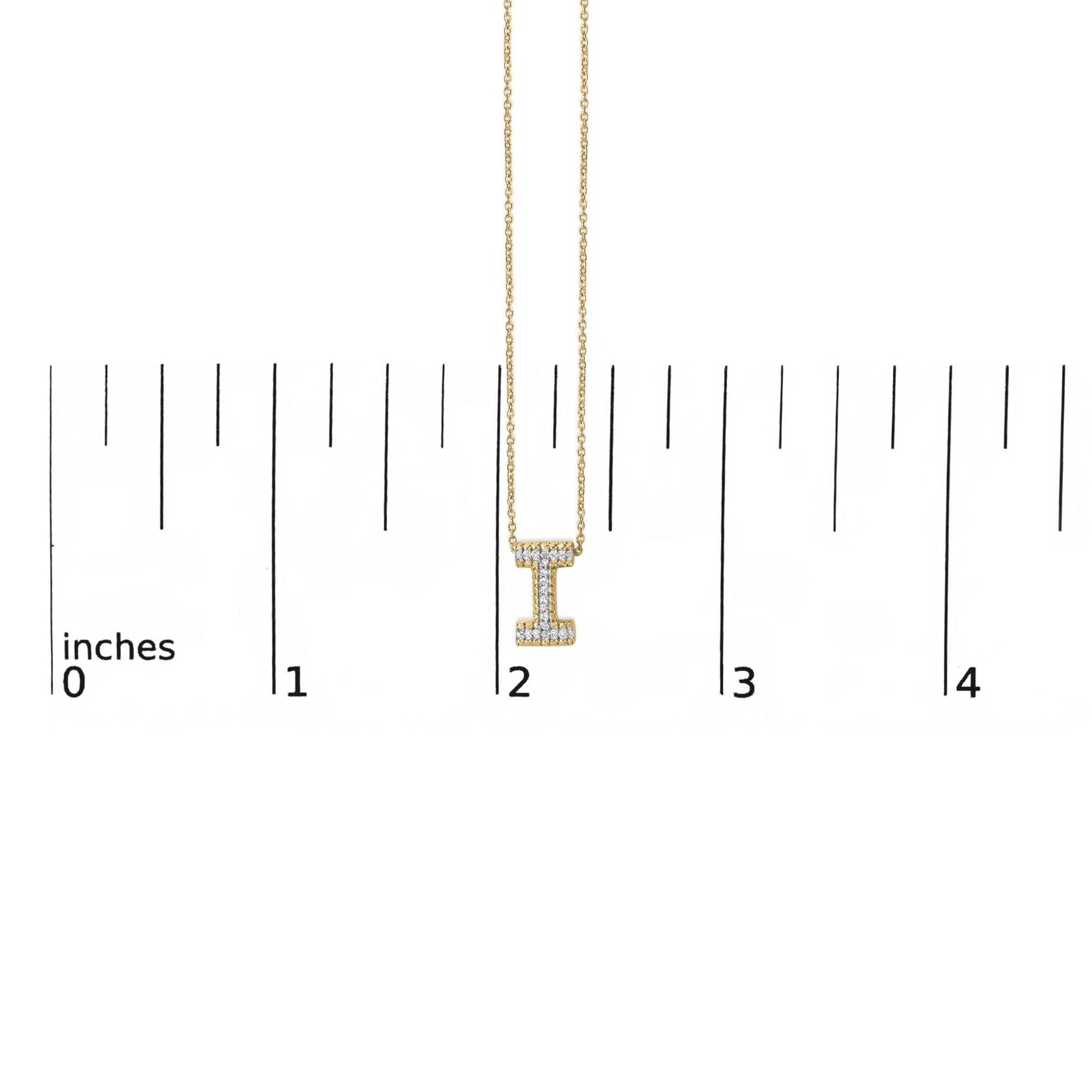 Close-up front view of a yellow metal necklace with a vertical bar pendant shaped like the letter 'I,' adorned with round white gemstones in a prong setting, shown on a scale with inch markings.