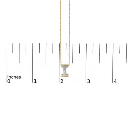 Close-up front view of a yellow metal necklace with a vertical bar pendant shaped like the letter 'I,' adorned with round white gemstones in a prong setting, shown on a scale with inch markings.