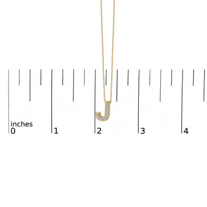 Close-up front view of a yellow metal necklace with a pendant in the shape of the letter J, featuring white round gemstones in a prong setting, shown on a ruler scale.
