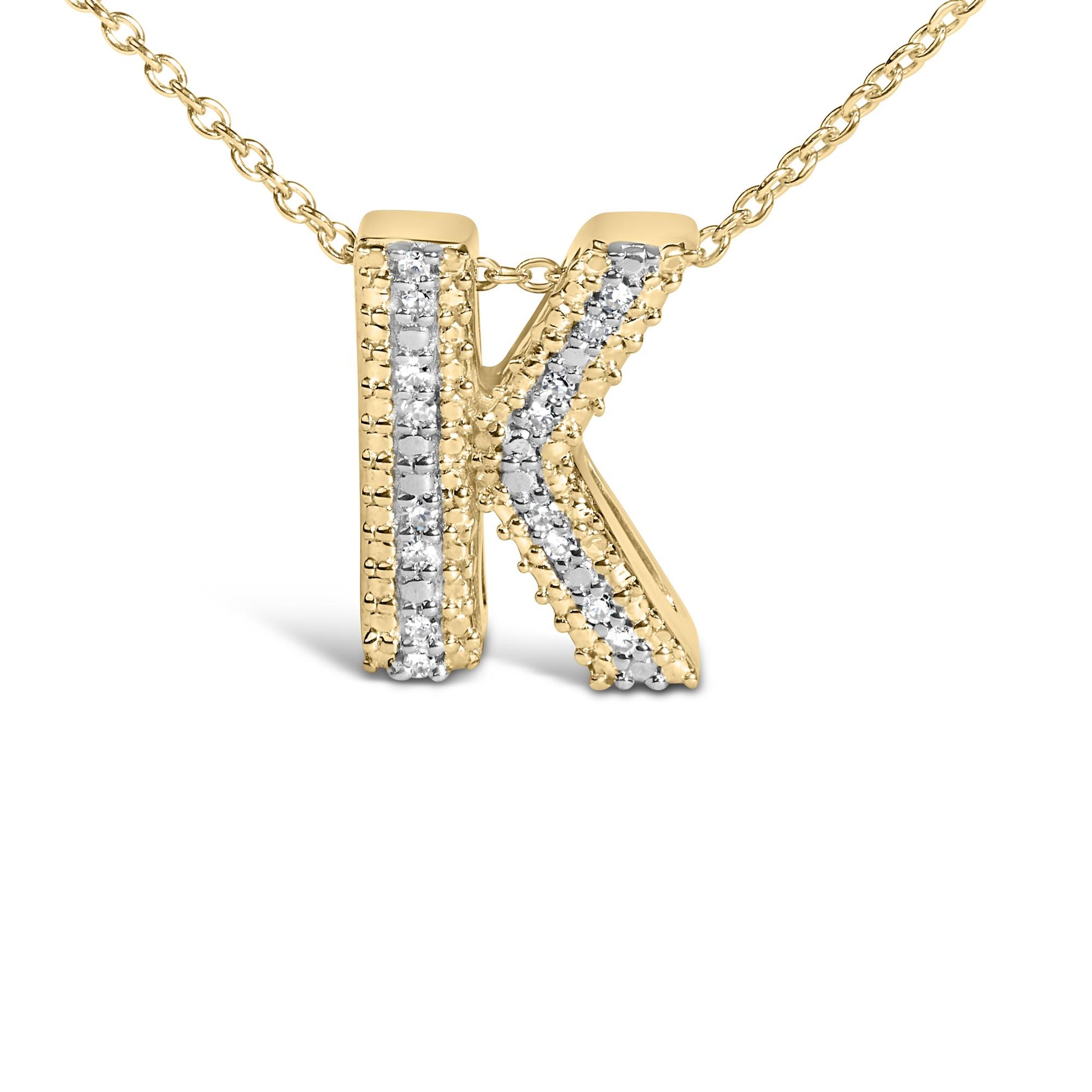 Close-up front angle of a yellow metal necklace pendant in the shape of the letter K, featuring two vertical lines of white gemstones in prong settings along its surface.