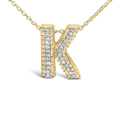 Close-up front angle of a yellow metal necklace pendant in the shape of the letter K, featuring two vertical lines of white gemstones in prong settings along its surface.