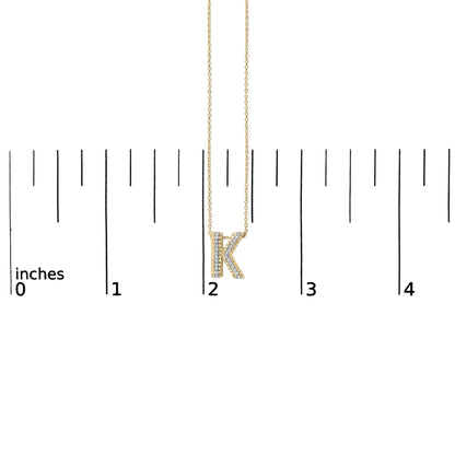 Close-up front view of a yellow necklace pendant in the shape of the letter K, adorned with white gemstones, shown hanging on a chain against a white background with measurement scale.