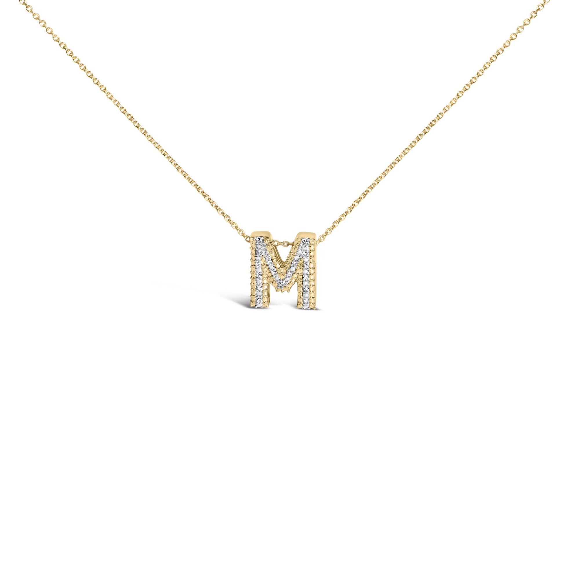 Close-up front view of a yellow metal necklace with an 'M' pendant adorned with prong-set white gemstones, shown on a white background.