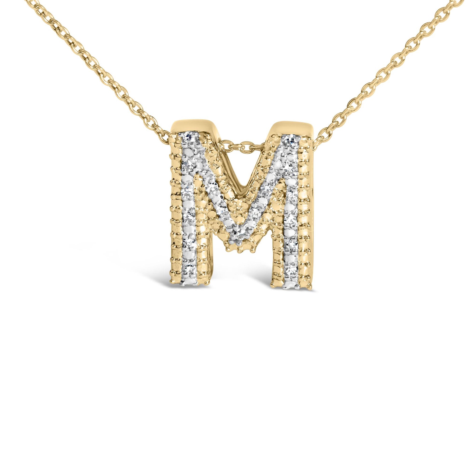 Close-up front view of a yellow metal necklace pendant in the shape of the letter 'M' adorned with white round gemstones in a prong setting, shown on a white background.