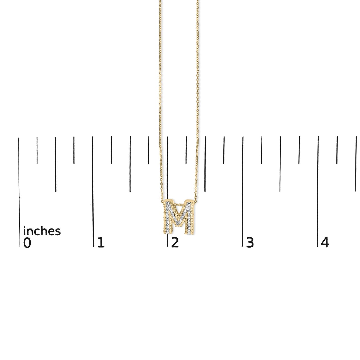 Close-up front view of a yellow metal necklace with an 'M' pendant adorned with white round gemstones in prong settings, shown on a scale.