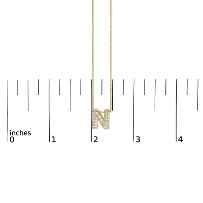 Close-up front view of a yellow necklace with a pendant shaped as the letter 'N' paved with white gemstones, shown on a measurement scale.