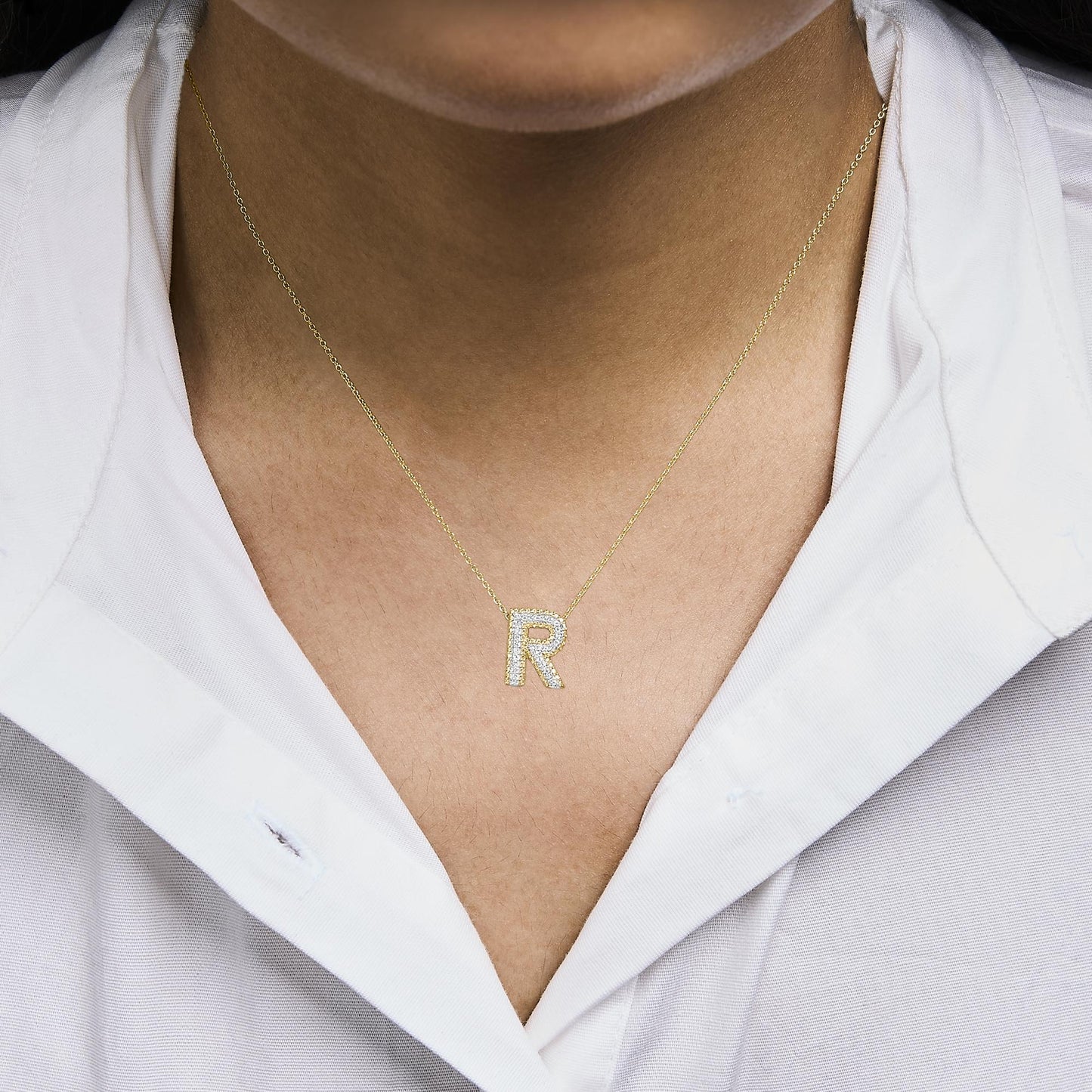 Close-up front view of a model wearing a yellow necklace with a pendant shaped as the letter 'R,' featuring white gemstones set in prongs.
