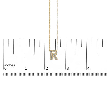 Image of a yellow metal necklace pendant shaped as the letter 'R' adorned with white gemstones in a prong setting, shown hanging on a chain against a ruler scale, viewed from the front.