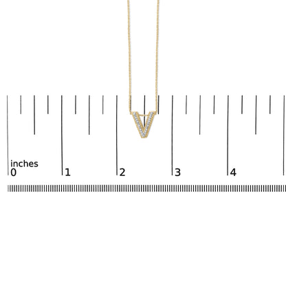 Yellow metal necklace with a V-shaped pendant set with white round gemstones in prong settings, shown on a scale from a front angle.