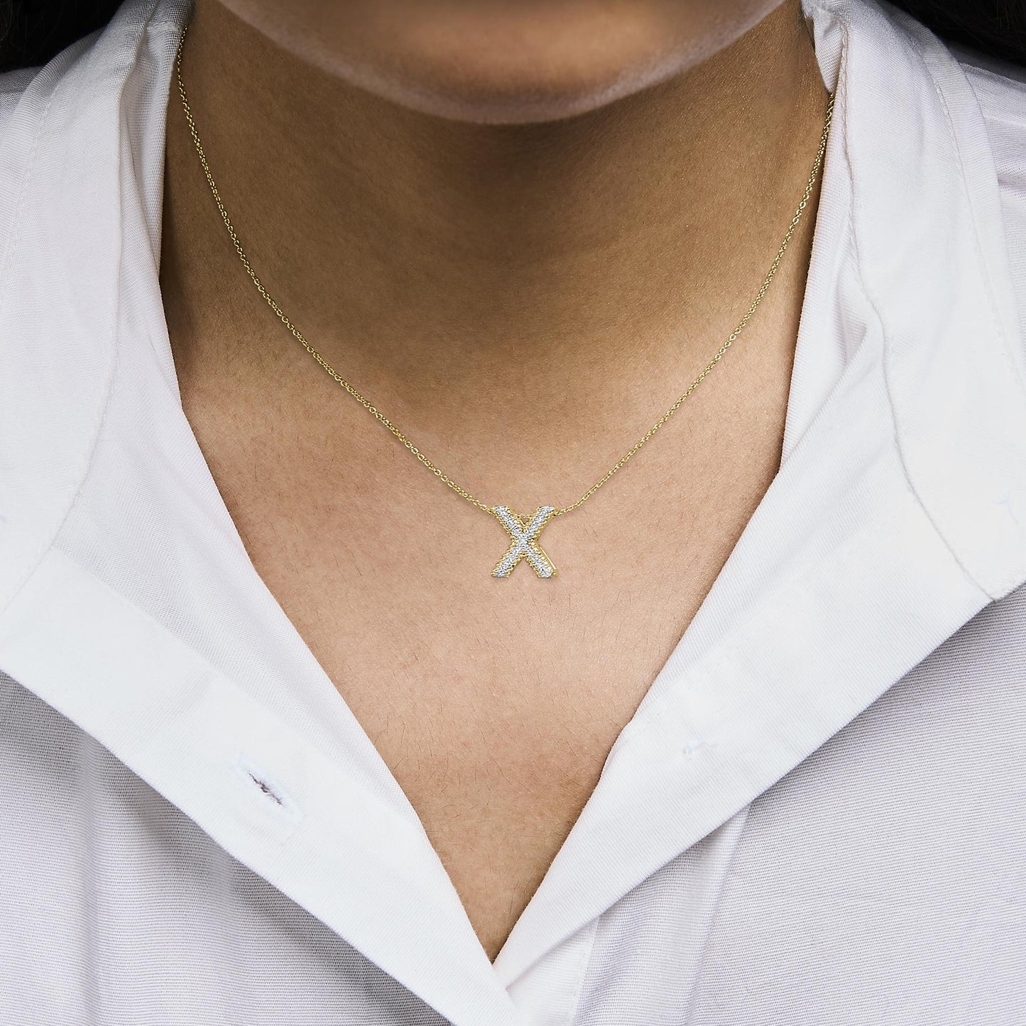 Close-up front angle of a model wearing a yellow metal necklace with an 'X' pendant encrusted with round white gemstones in prong settings.