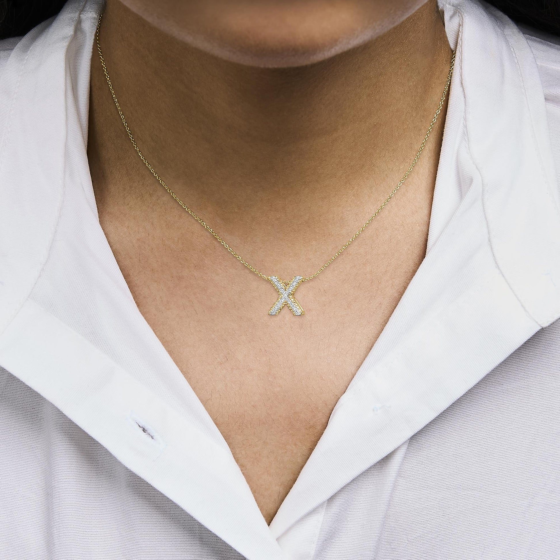 Close-up front angle of a model wearing a yellow metal necklace with an 'X' pendant encrusted with round white gemstones in prong settings.