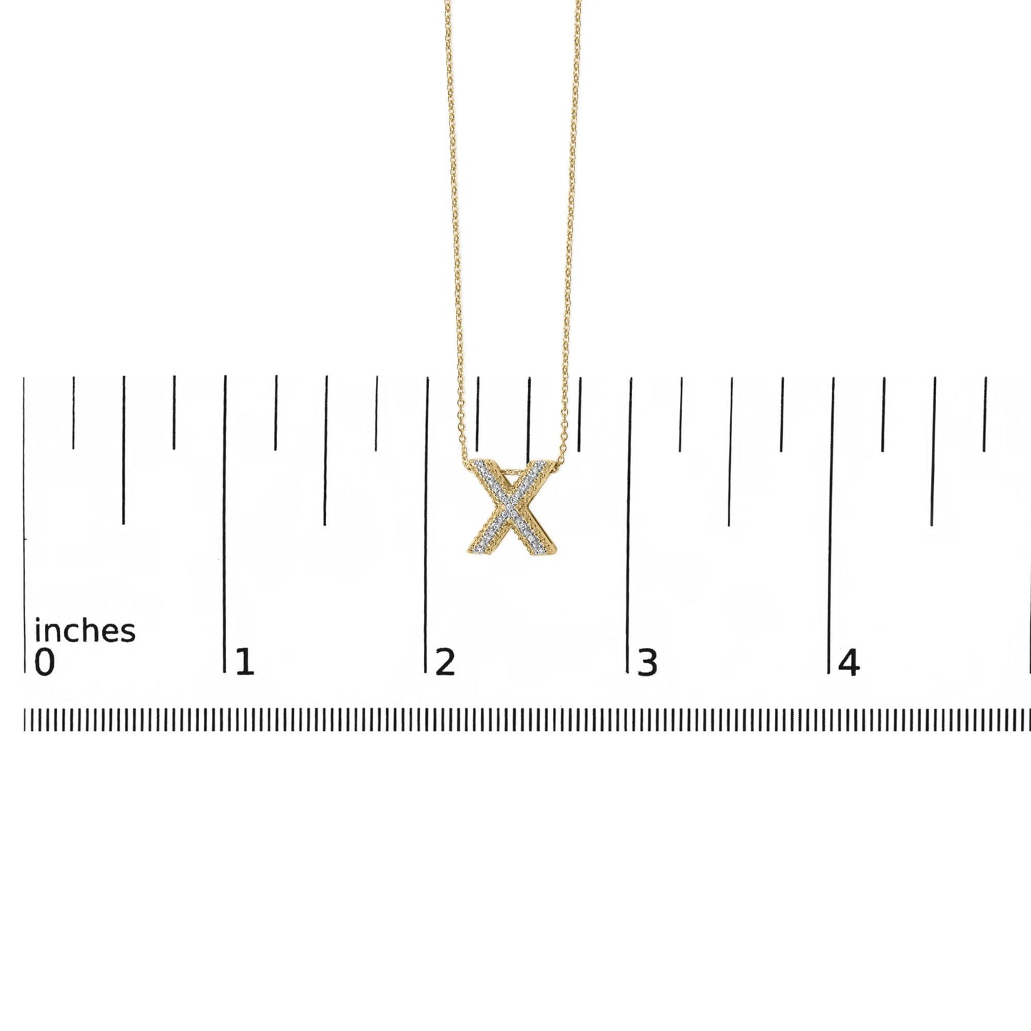 Yellow metal necklace with an X-shaped pendant featuring white round gemstones in a prong setting, shown hanging against a ruler scale, front view.
