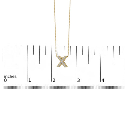Yellow metal necklace with an X-shaped pendant featuring white round gemstones in a prong setting, shown hanging against a ruler scale, front view.