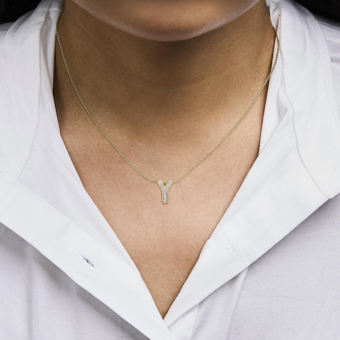 Close-up front view of a model wearing a yellow metal necklace with a Y-shaped pendant adorned with prong-set round white gemstones.