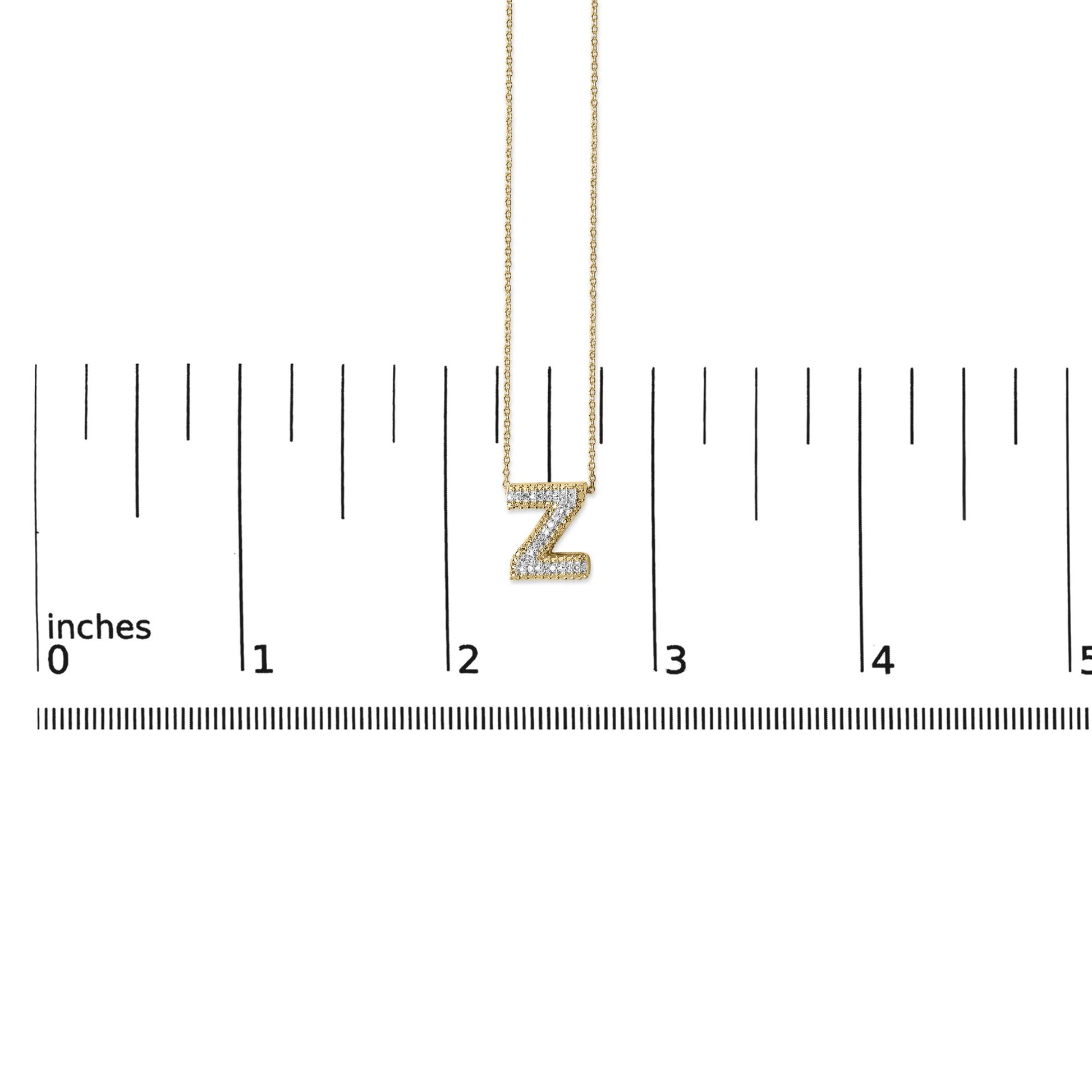 Yellow metal necklace with a 'Z' pendant encrusted with white gemstones in a prong setting, shown on a ruler scale from a front angle.