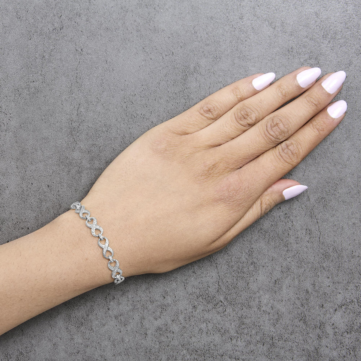 Bracelet with white metal and white round gemstones in pave setting, forming an infinity design, shown worn on a model's wrist from a top angle.