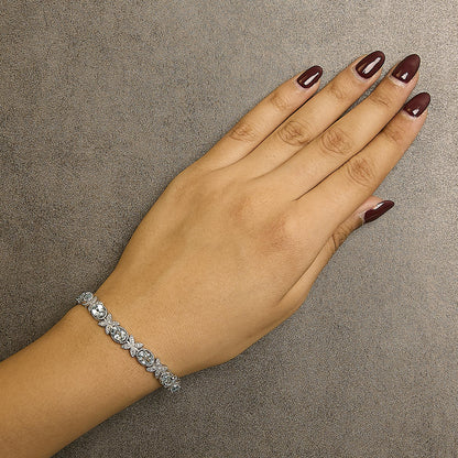White metal bracelet with alternating oval blue gemstones in prong settings and round white gemstones in pave settings, shown on a model's wrist from an overhead angle.