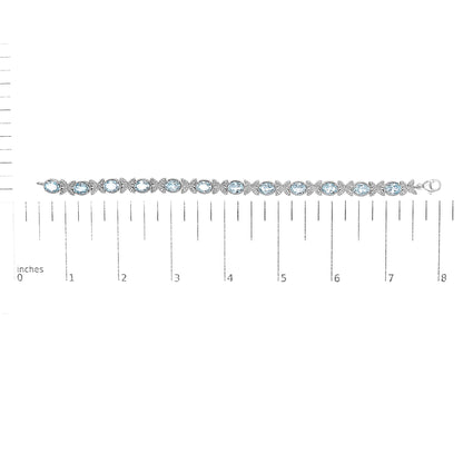 White metal bracelet with alternating oval blue gemstones and round white gemstones in pave setting, laid flat on a ruler for size reference, top-down view.